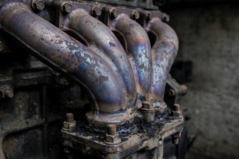 Cast-iron exhaust manifold on a diesel generator engine showing heat discoloration on the runners — thermal cycling is what cracks them